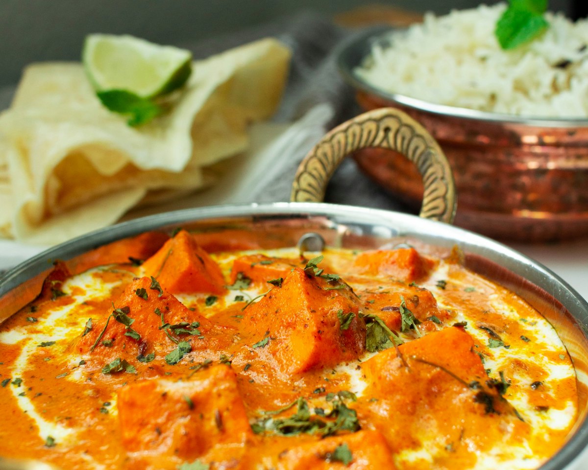 Butter chicken in a copper karahi with rice and naan